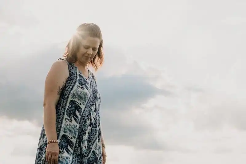 Portrait of a woman in a flowy dress with a cloudy sky background.