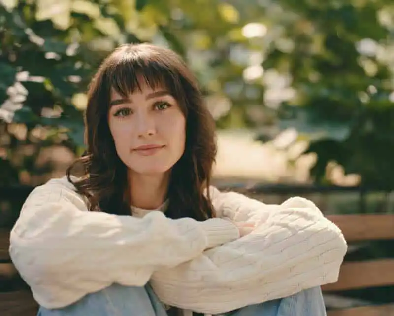 Portrait of a woman with brown hair and gentle expression in a park setting.