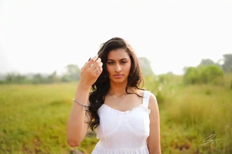 Beautiful woman in a white dress standing outdoors with greenery in the background.