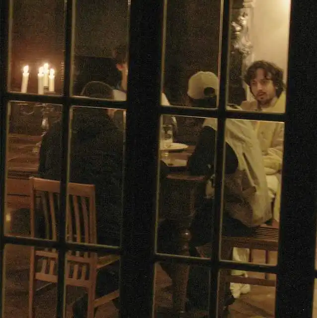 A warm, intimate restaurant setting with patrons enjoying dinner. The scene highlights a cozy ambiance with candlelight and reflective glass.