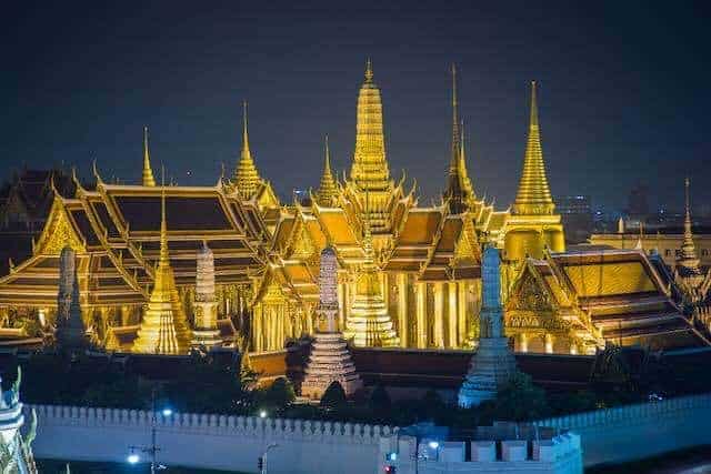 Night view of illuminated Thai temples with golden spires in Bangkok.