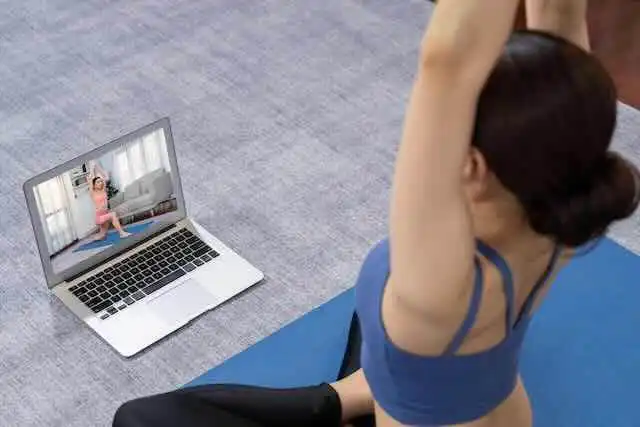 Young woman practicing yoga via online class on laptop.